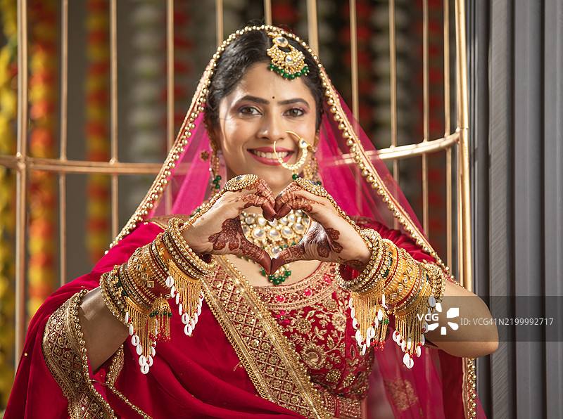 身穿红色婚纱的幸福新娘做出心形手势图片素材