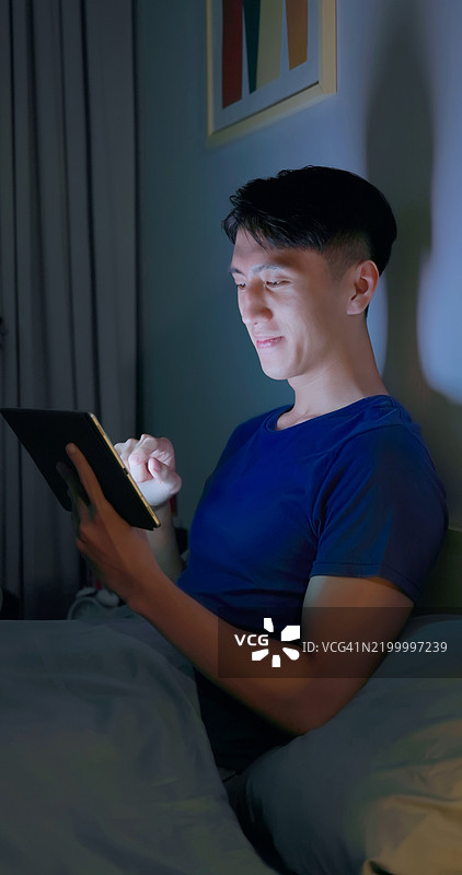 黑暗中 scrolling 平板电脑的男人图片素材