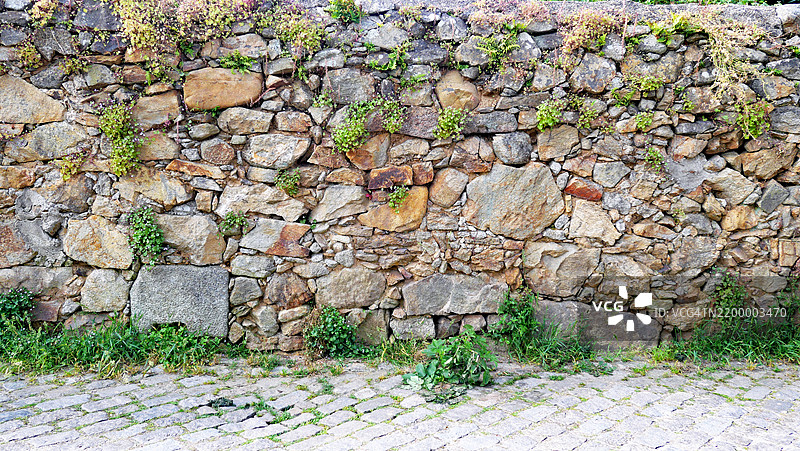葡萄牙的棕色和灰色风化石墙，绿植环绕，鹅卵石街道。图片素材
