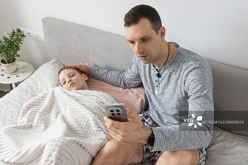 智能手机应用指导儿童睡眠健康评估。细心的单身爸爸在夜间远程医疗会议中监测症状。图片素材