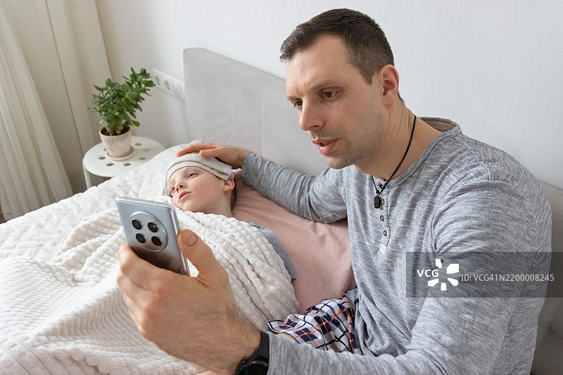 医疗咨询通过智能手机屏幕进行。专注的父母在虚拟医生就诊期间监控休息中的孩子。图片素材