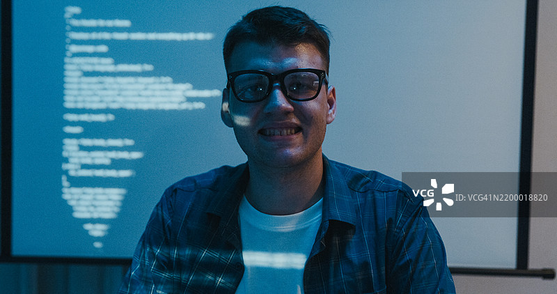 年轻美国男性IT专业人士数据科学家在办公室夜晚加班时微笑着工作，专注于人工智能和编程。图片素材