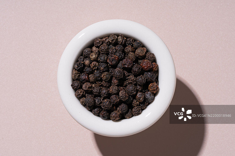 米色背景上的黑胡椒粒碗图片素材