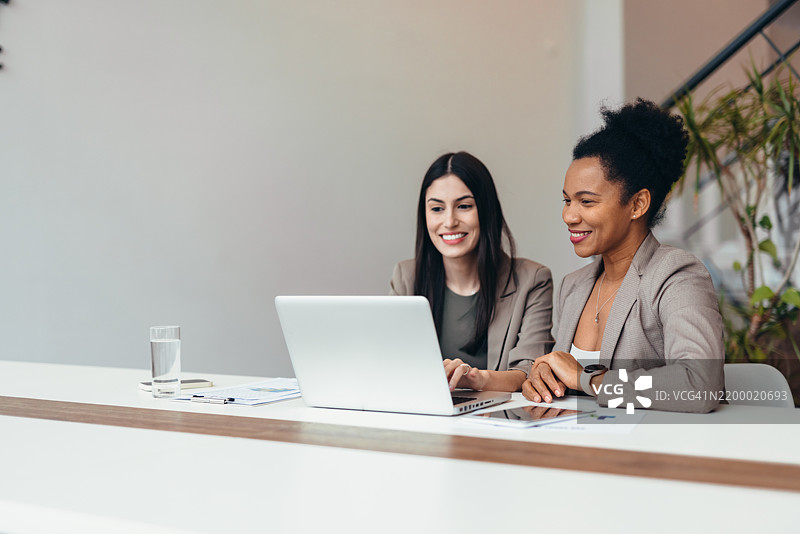 两位女商人在办公室微笑着使用笔记本电脑工作图片素材