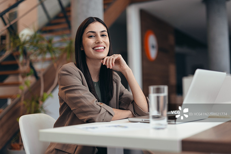年轻女商人在现代办公室微笑着使用笔记本电脑图片素材