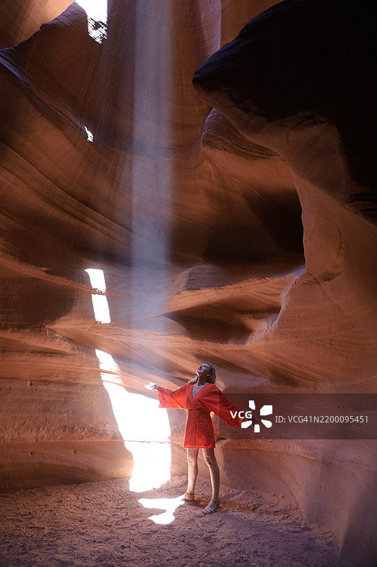 穿着红色裙子的美丽女人在洞穴中玩光影图片素材