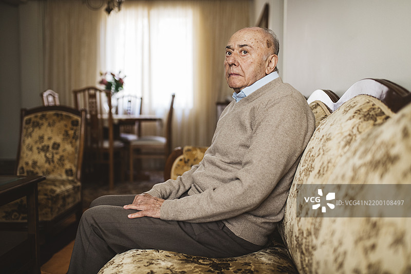一位老年男子安静地坐在舒适房间的花纹沙发上图片素材