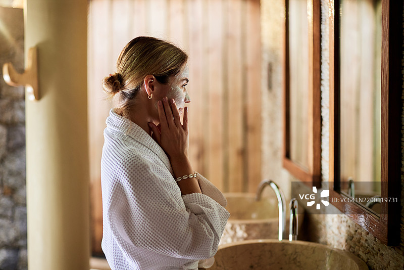 微笑的女性在浴室里早晨涂抹保湿霜。图片素材