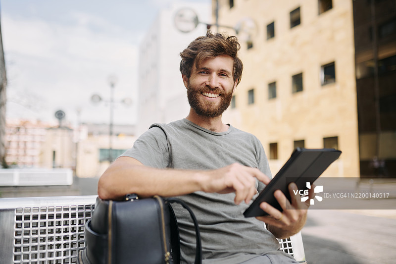 在城市户外，背着背包的男子正在使用应用程序查看住宿预订。快乐的男性游客利用数字技术和在线语言翻译在城镇中探索。图片素材