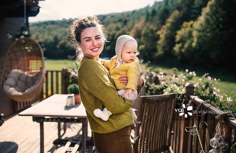 美丽年轻母亲与小女儿的肖像，站在阳台上欣赏周围的自然景色。图片素材