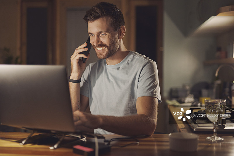 远程工作，电话沟通，微笑的男子与笔记本电脑进行虚拟咨询，解决技术问题或更新系统。网络管理员，自由职业者或夜班工作者在家中与客户联系。图片素材