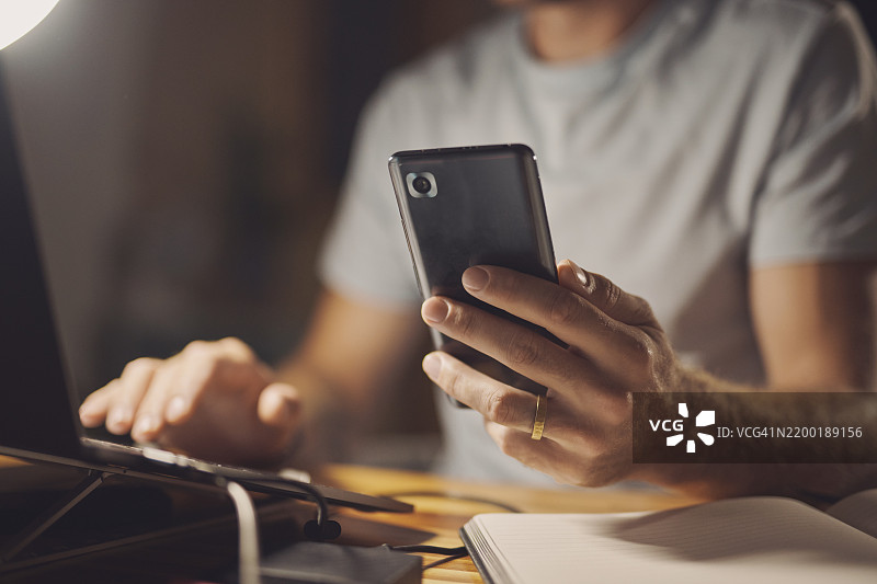 笔记本电脑、夜晚或男人在办公室用手机的手，适用于刑事案件、证据或公司政策审查。研究、特写镜头和加班侦探使用技术、笔记本日记或移动应用。图片素材