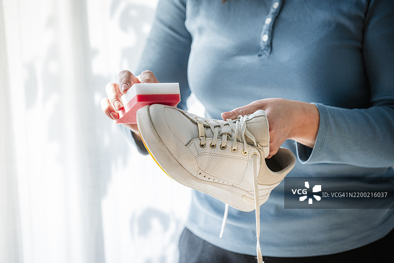 一位无法辨认的女性在家中用特殊清洁海绵擦拭白色运动鞋图片素材