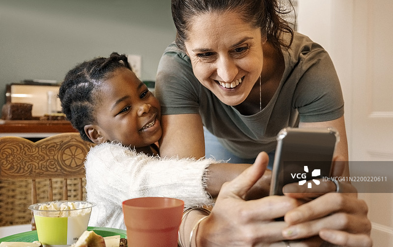 母亲和养女在餐桌前微笑着，手里拿着手机图片素材