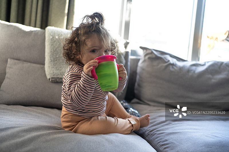 卷发宝宝在沙发上用吸管杯喝水图片素材