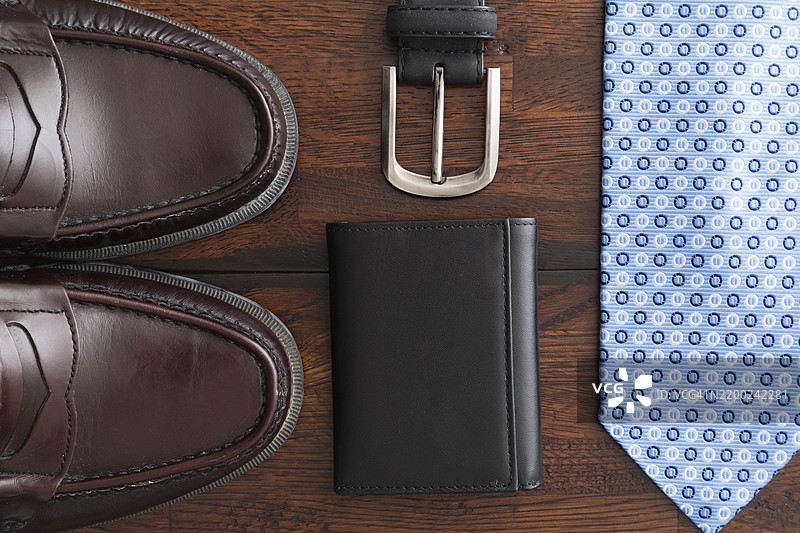 时尚的正式配饰，包括鞋子、钱包、领带和皮带，整齐地摆放在木质表面上图片素材