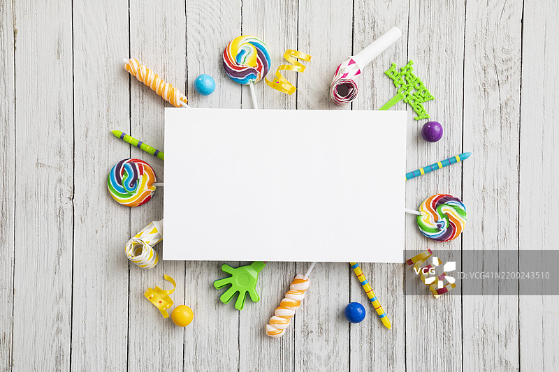 五彩缤纷的糖果和装饰品环绕着一张空白卡片，摆放在木桌上，营造出节日庆祝的氛围。图片素材