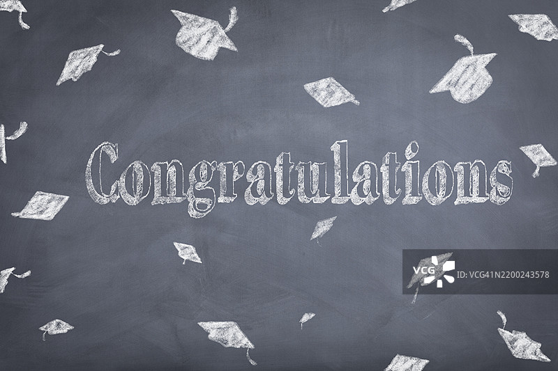 毕业庆典上，黑板背景上写着的祝贺信息，旁边有毕业帽。图片素材