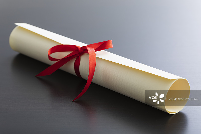 毕业典礼后，桌子上放着卷起并用红色丝带系好的文凭图片素材