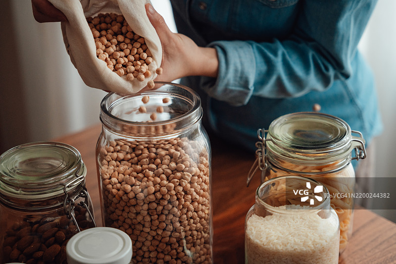 年轻女性将散装购买的鹰嘴豆放入玻璃容器中的特写镜头图片素材