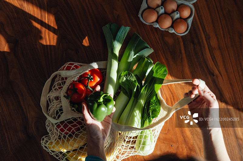女性手平铺在桌面上，从可重复使用的购物袋中取出新鲜的水果和蔬菜图片素材