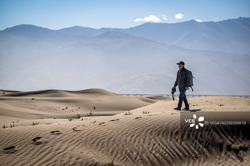 男性徒步旅行者在沙漠中的沙丘上行走，留下沙地上的脚印。哈密，新疆，中国图片素材