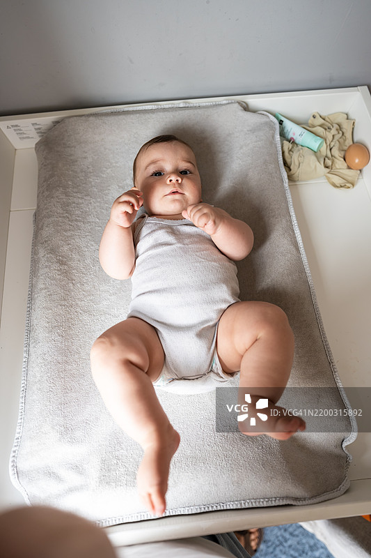 婴儿躺在换尿布台上，注视着镜头图片素材
