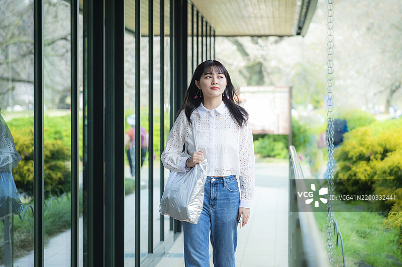 年轻女性手提银色手提包走在玻璃墙旁图片素材