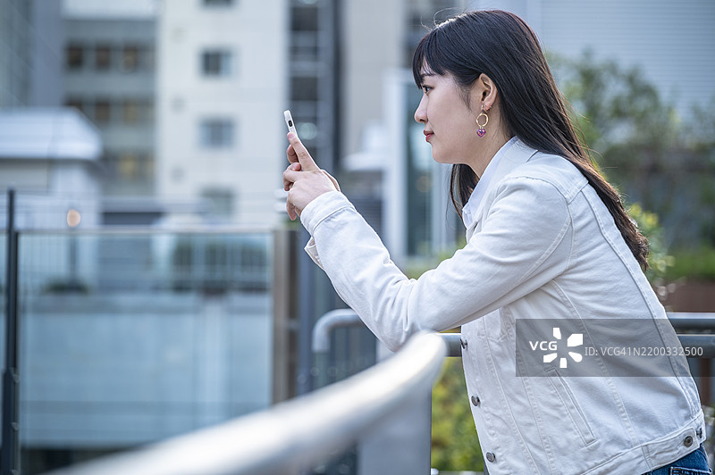 年轻女性在日落时分的户外阳台上使用智能手机图片素材