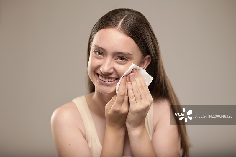 女孩在工作室里开心地使用化妆品和湿巾，背景适合肖像拍摄，体现卫生或转变。青少年、人物和模特微笑着用化妆棉清洁肌肤，关注护肤、污垢或皮肤科。图片素材