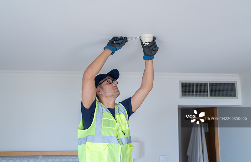 工人在酒店房间天花板上安装烟雾探测器图片素材
