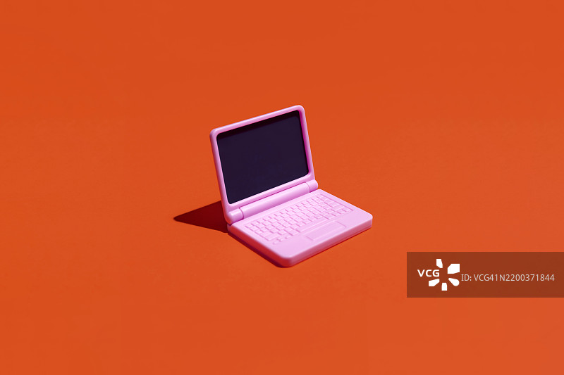 粉色笔记本电脑放在鲜艳的橙色背景上图片素材