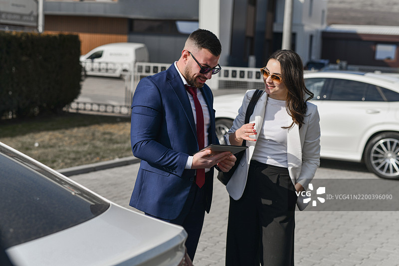 男士穿着正式服装，向女性客户展示数字平板上的文件，以完成购车流程。图片素材