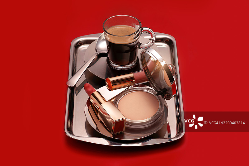 抽象创意概念的礼物或早晨化妆例程，由时尚美容化妆品为女性制作，银色托盘上放着咖啡杯和勺子，背景为红色。图片素材