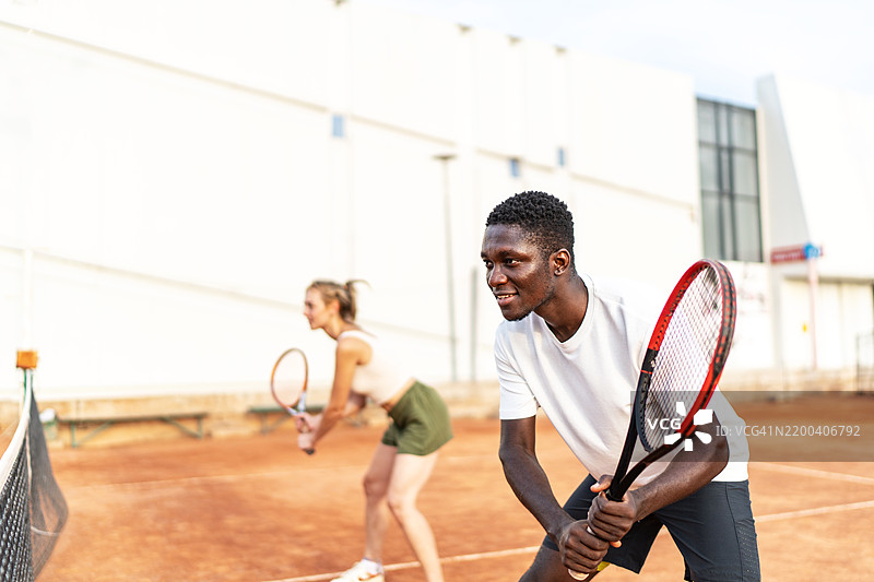 年轻男女在户外的红土网球场上打双打网球图片素材