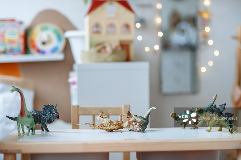 五颜六色的恐龙玩具杂乱地摆放在明亮的儿童房间的桌子上，没有人。图片素材