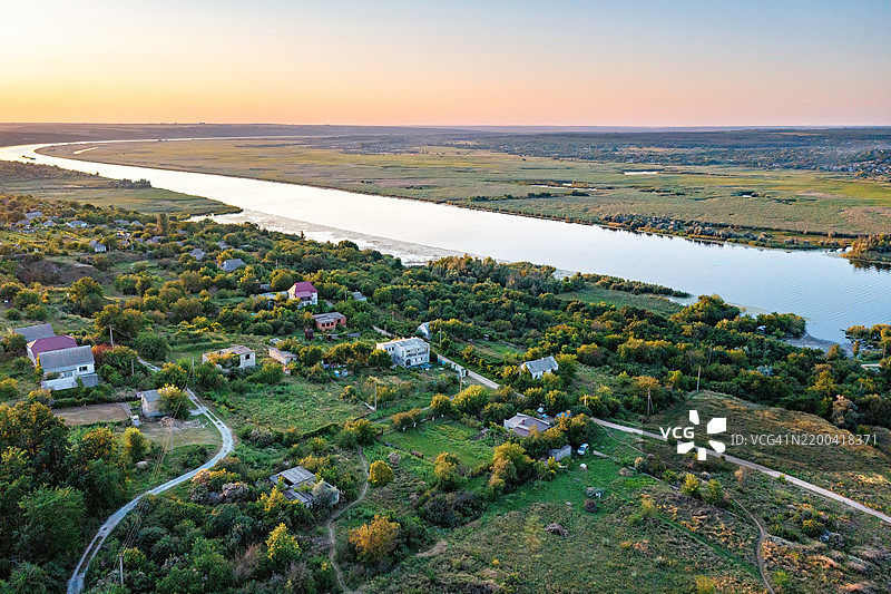 日落时分的风景如画的河边景观展现了宁静的村庄和郁郁葱葱的绿意 航拍照片图片素材