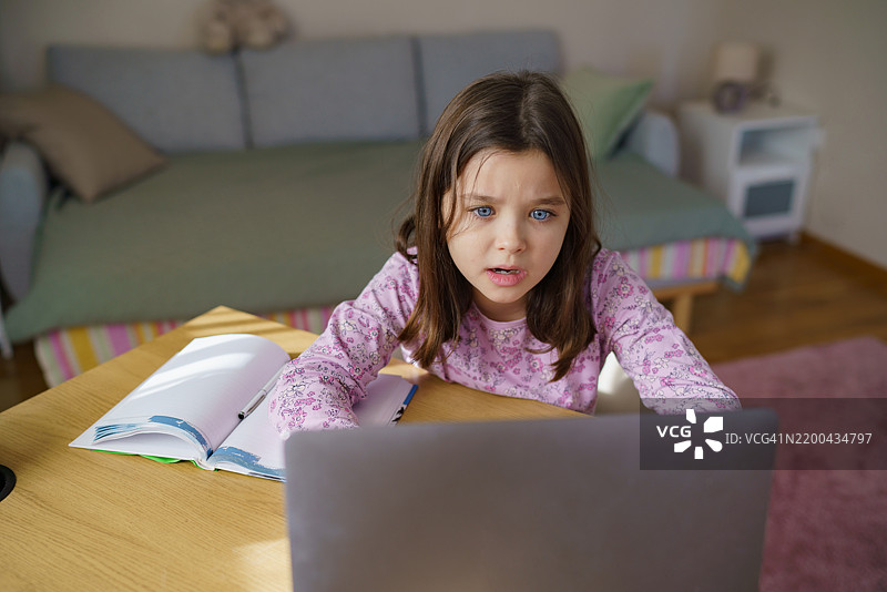 小女孩在做作业时惊讶地看着笔记本电脑图片素材