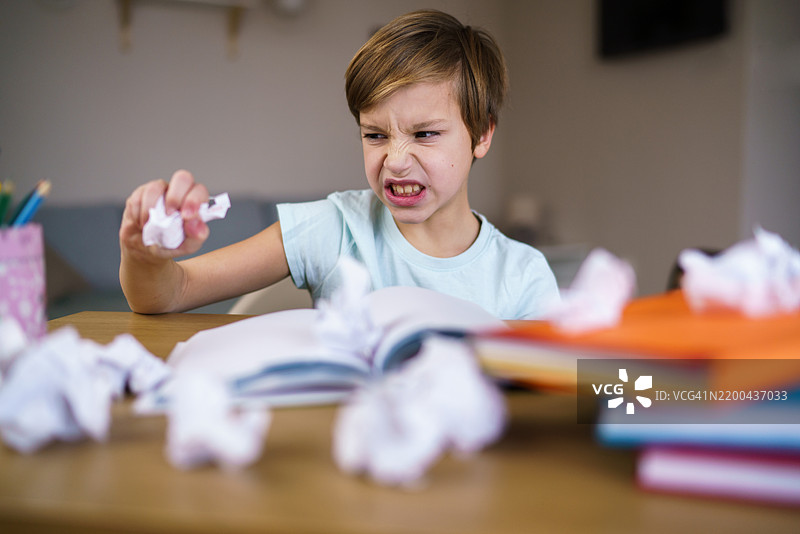 一个生气的男孩在写故事时把纸揉成一团图片素材