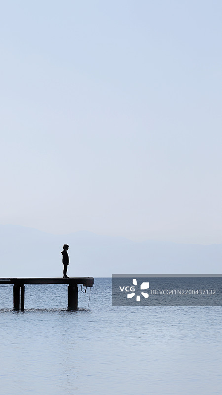 男人站在海边的码头上，背对着天空。图片素材