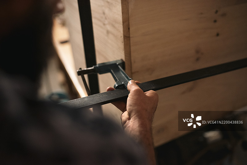 一名男子在木工车间使用夹具进行木材加工的背影图片素材