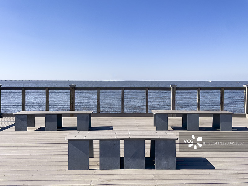 三张简约的长椅位于带栏杆的公共甲板上，俯瞰着宽阔的湖泊。图片素材