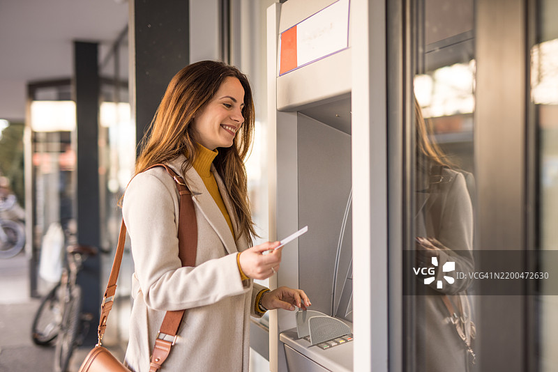 年轻女性在城市街道的ATM机上取款图片素材