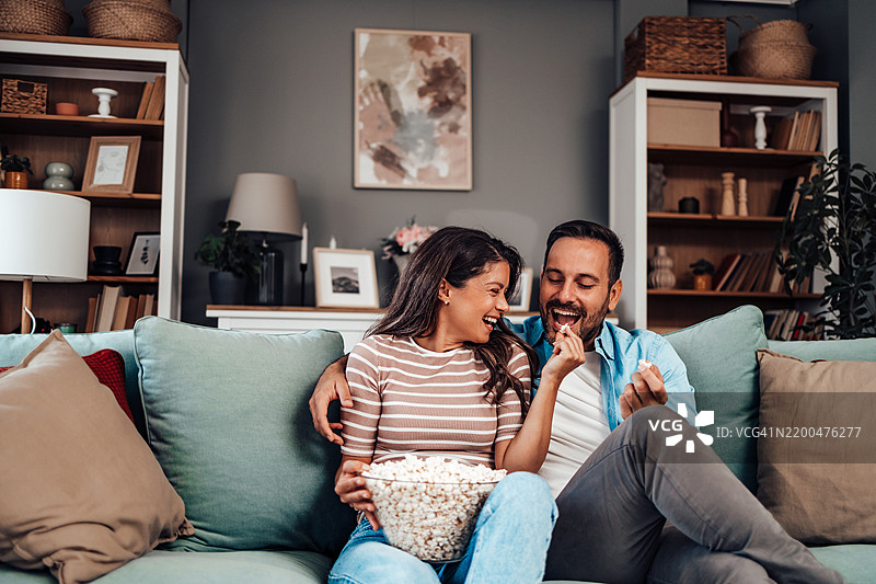 每日一剂浪漫。年轻情侣享受电影、爆米花和沙发的舒适。图片素材