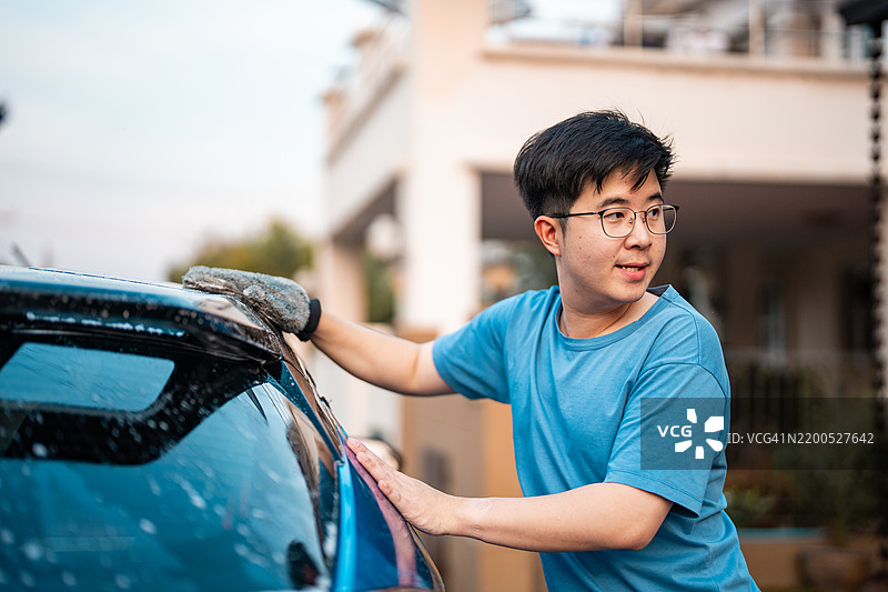 一名年轻男子正在用肥皂和水清洗他的汽车。图片素材