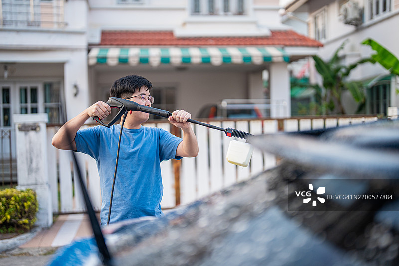在他家门前，一位中年亚洲男子正在清洗和洗涤他的汽车。图片素材