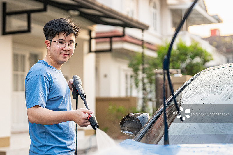 在他家门前，一位中年亚洲男子正在清洗和洗涤他的汽车。图片素材
