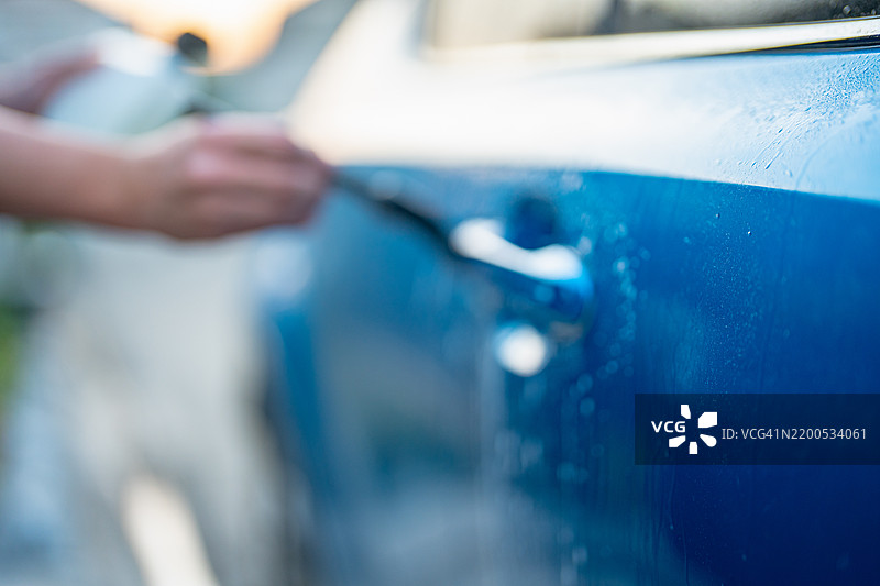 在他家门前，一位亚洲成年男子正在清洗他的汽车。图片素材