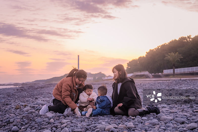 亚洲家庭朋友，母亲和儿子坐在一起放松，探索旅行度假，享受交谈并一起照顾她的宝宝，夕阳下的美好时光。图片素材