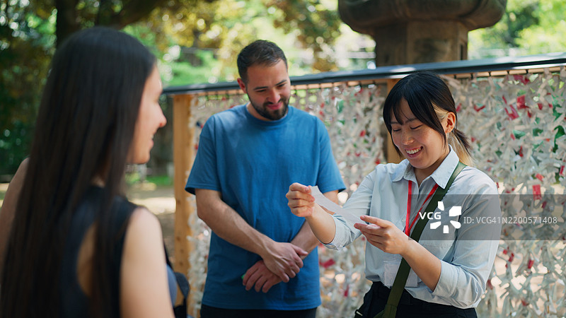 一位亚洲女性导游在日本神社为游客阅读和解释日本的签文（御御签）图片素材